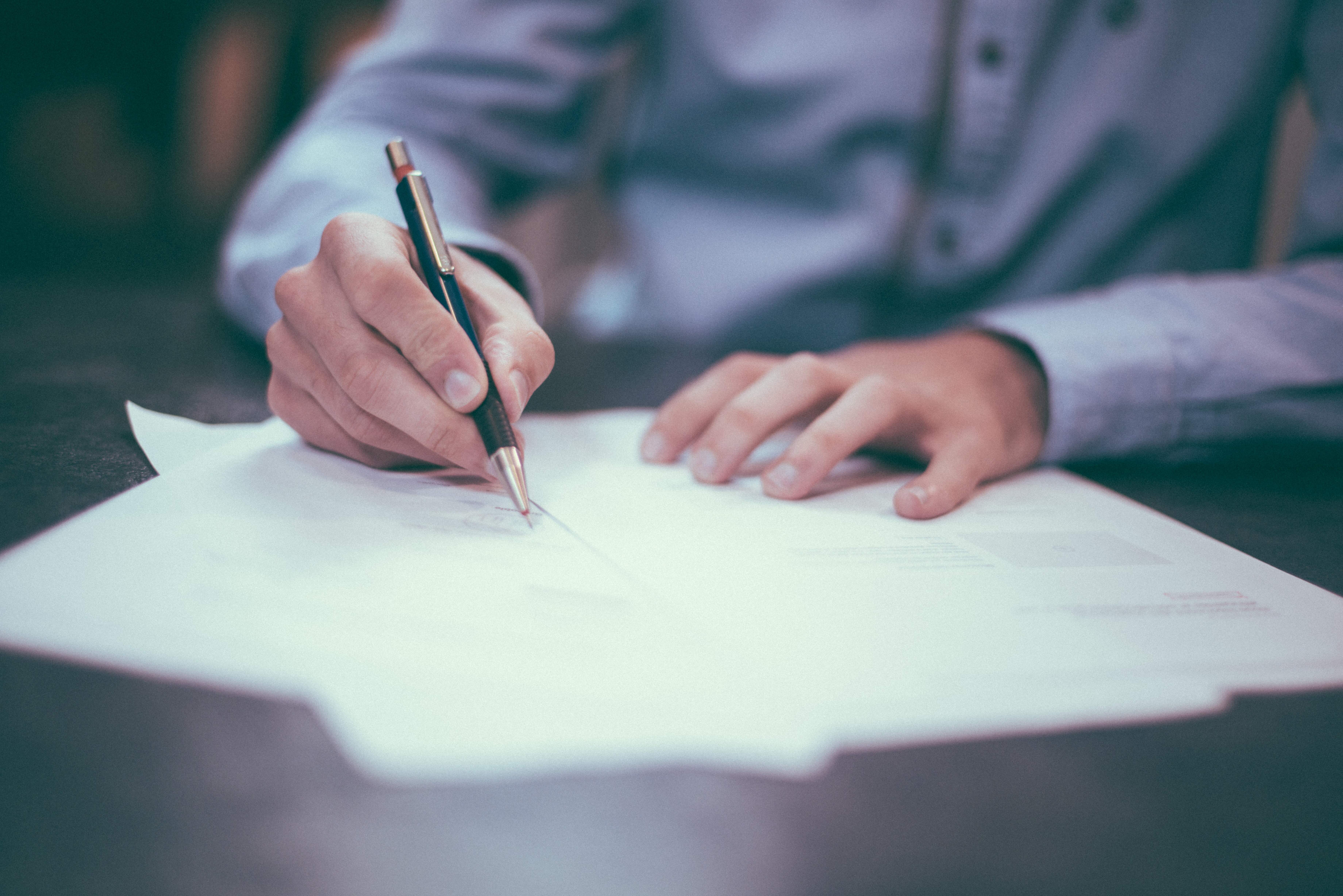 Hombre sentado en una mesa firmando un contrato de trabajo cumpliendo con el mínimo de 6 meses de relaciones laborales con anterioridad a su solicitud de arraigo laboral