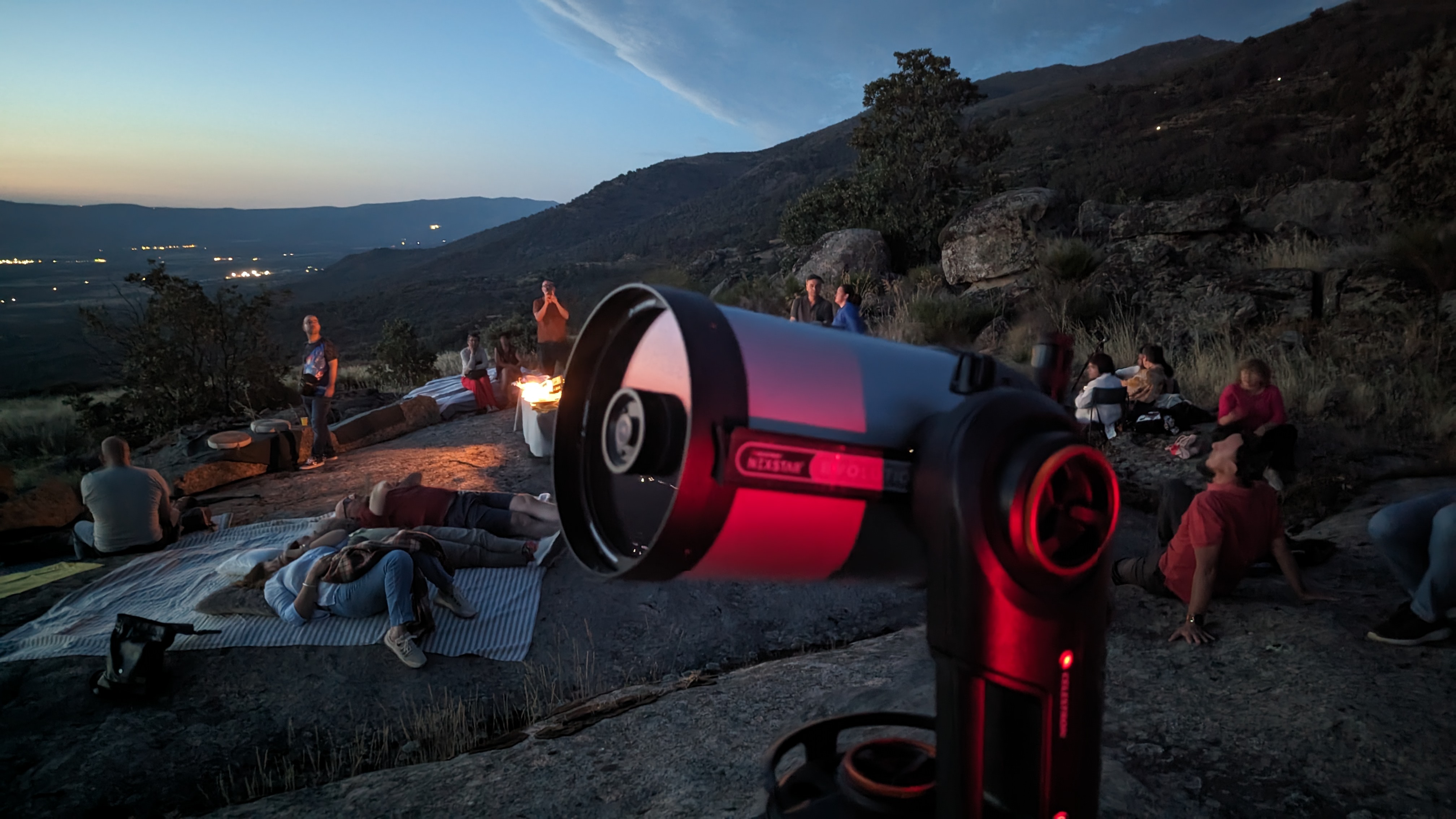 Grupo de personas al atardecer en la montaña y un telescopio de alta gama en primer plano
