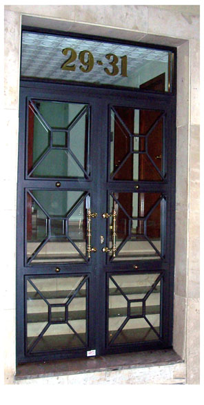 Puerta de comuidad de hierro con motivos geometricos y manillones y detalles de latón