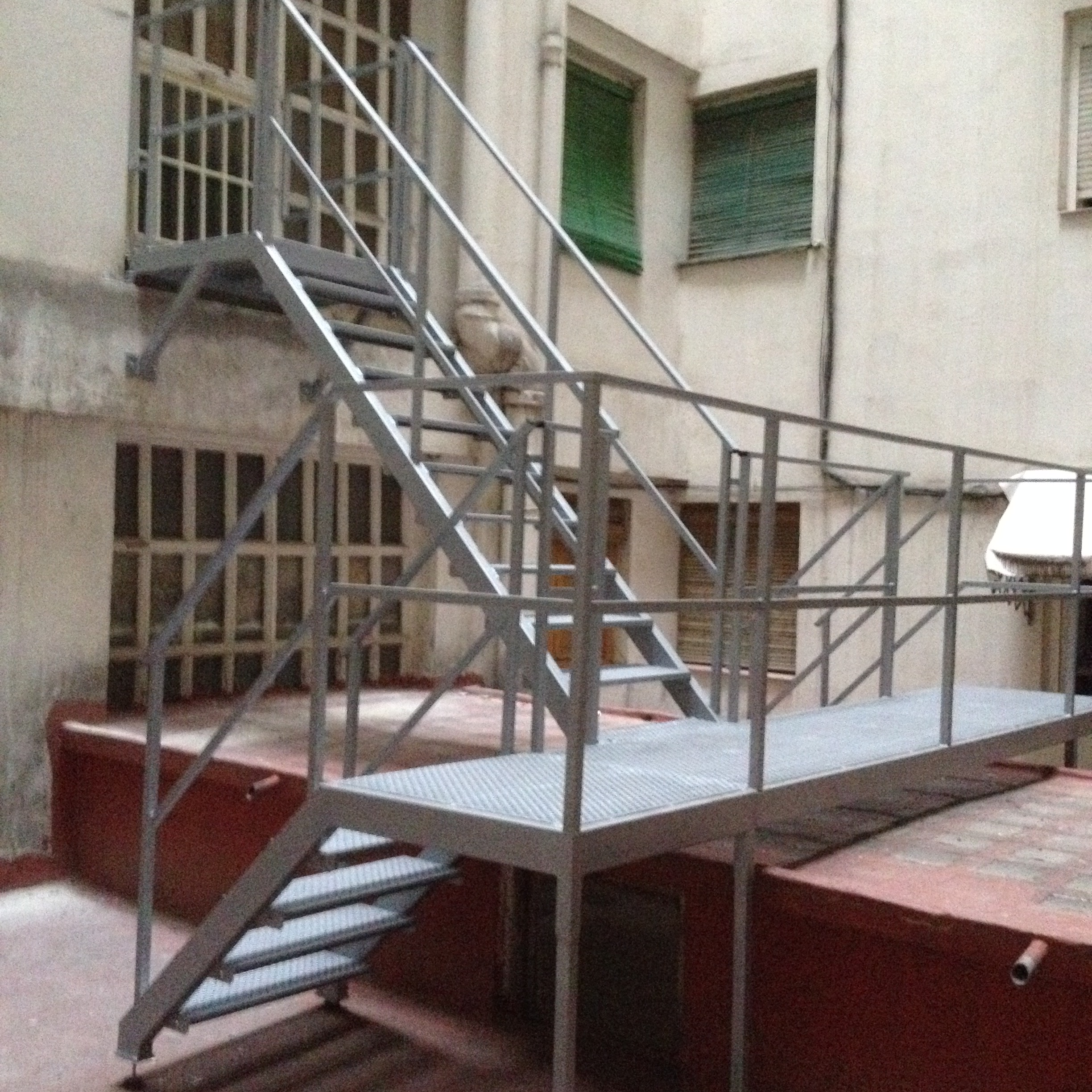 Escalera y plataforma de hierro en comunidad con pisas y suelo de plataforma de chapa antideslizante y barandilla de perfil tubular