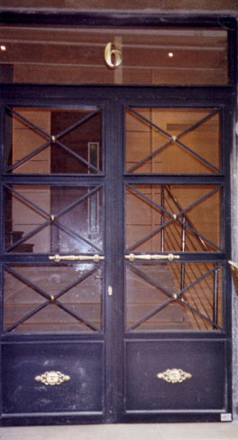Puerta de comunidad con motivos geometricos en forma de aspa, manillones y detalles de latón.