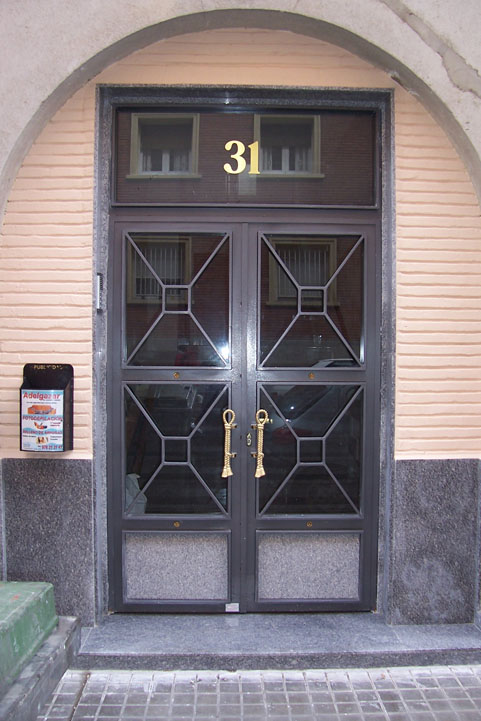 Puerta de comunidad de hierro y marmol con detalles geometricos y detalles y manillones de latón.