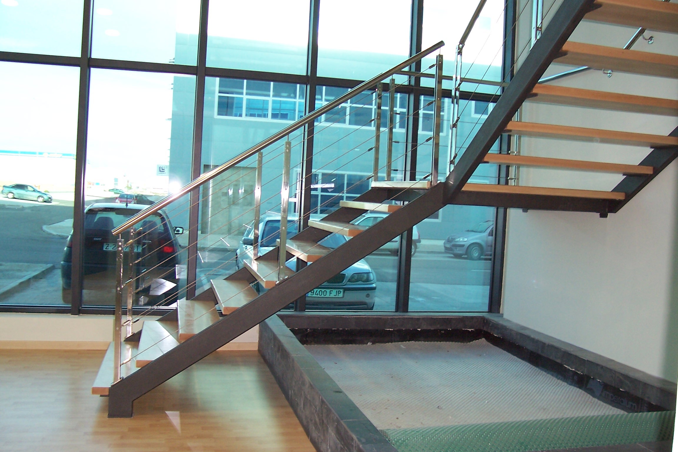 Escalera metalica con pisas de madera y barandilla de acero inoxidable de cables y zancas de tubo de hierrro