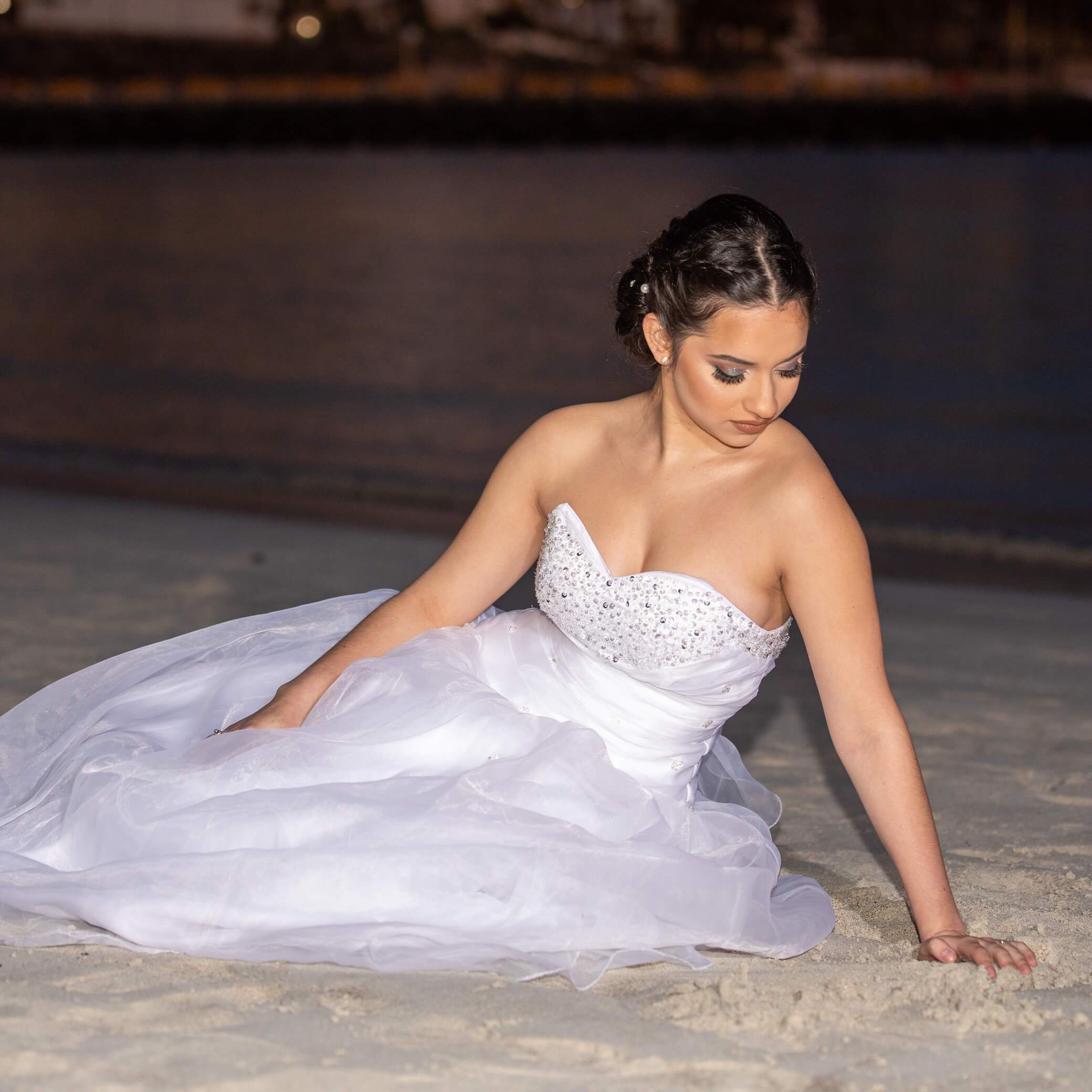 Foto de una chica vestida de blanco y sentada en la arena mientras es fotografiada